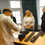 Ein Projektteilnehmer erläutert Staatsministerin Petra Köpping und Sozialbürgermeisterin Vicki Felthaus Arbeiten an einer Modelleisenbahn für Außenbereiche, die in der S.A.V.E. Projektwerkstatt instandgesetzt wird.